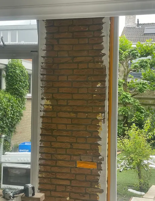 Een gemetselde bakstenen stijl tussen twee glazen puien, met de tuin erachter