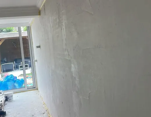 Een pas gestucte, gladde wand in een ruimte die nog niet af is, met links een glazen pui