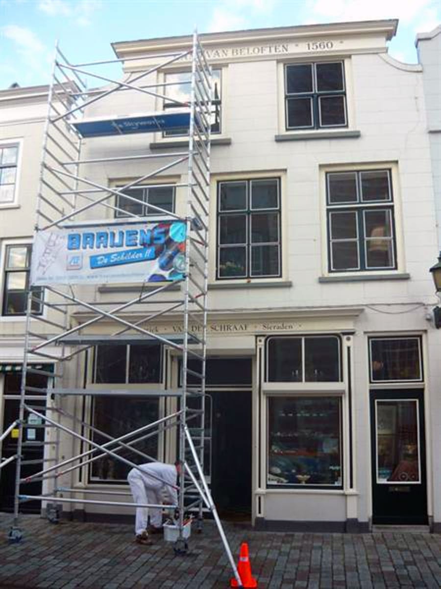 Rolsteiger met een banner van Baaijens tegen een monumentale gevel, met een schilder in witte werkkleding aan de voet.