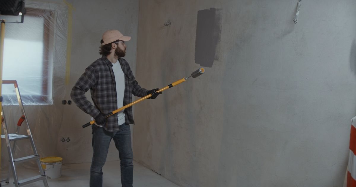 Schilder brengt met een rol op een lange steel een laag verf aan op een kale wand.