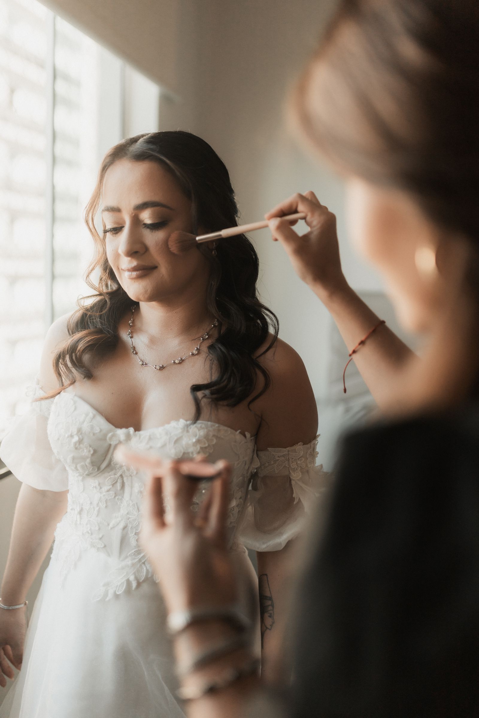 Een bruid krijgt in zacht daglicht haar make-up aangebracht