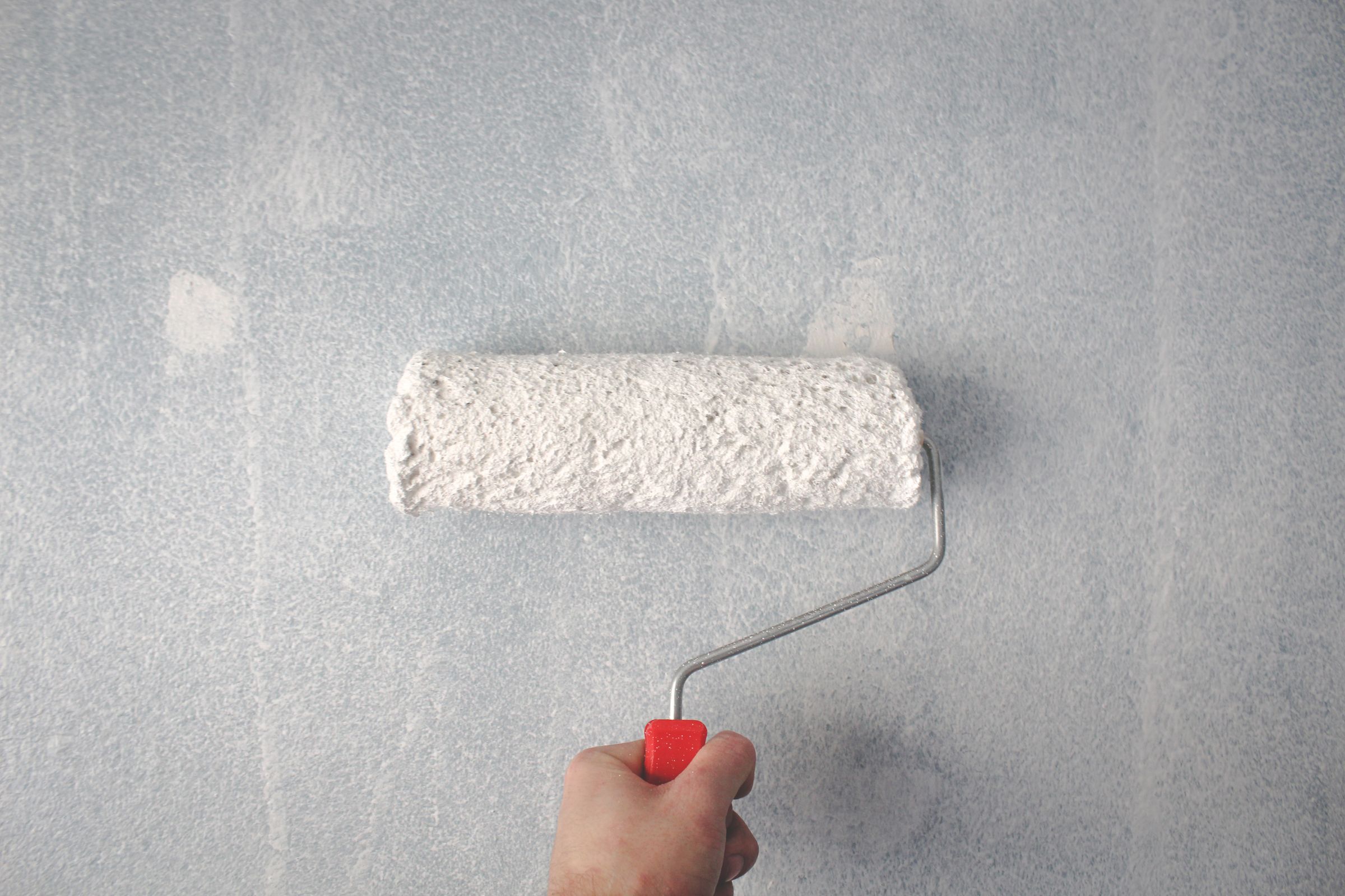 Een hand rolt met een verfroller een nieuwe laag witte verf op een wand