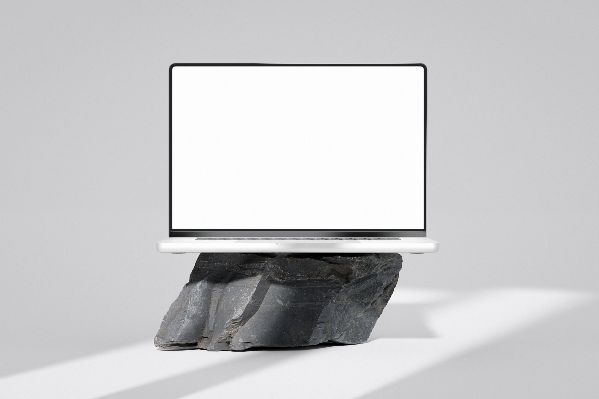 Een laptop met een leeg scherm, gefotografeerd op een ruw stuk steen tegen een lichte studioachtergrond