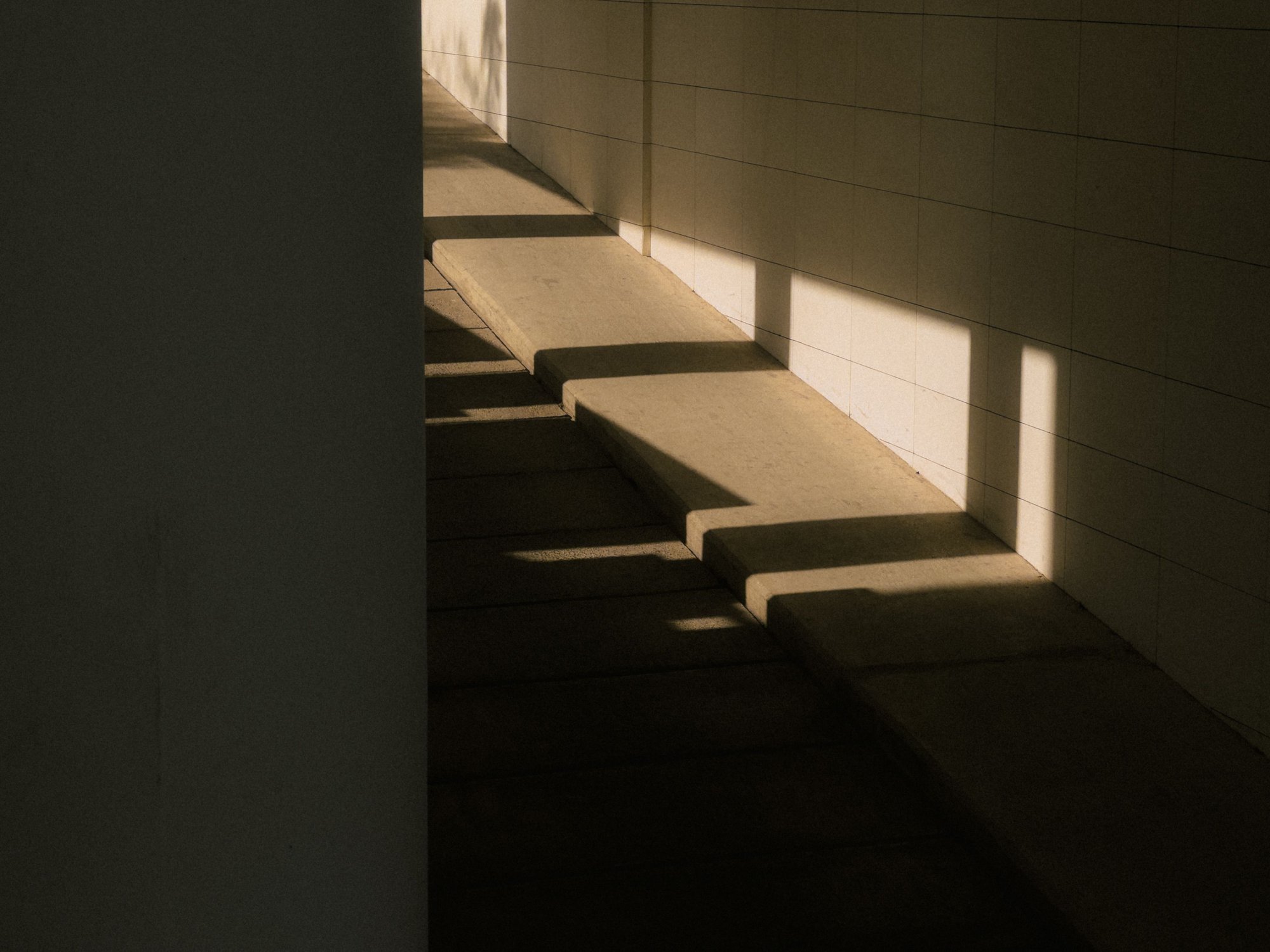 Strijklicht dat door een gang valt en scherpe schaduwen tekent op een trap en een muur