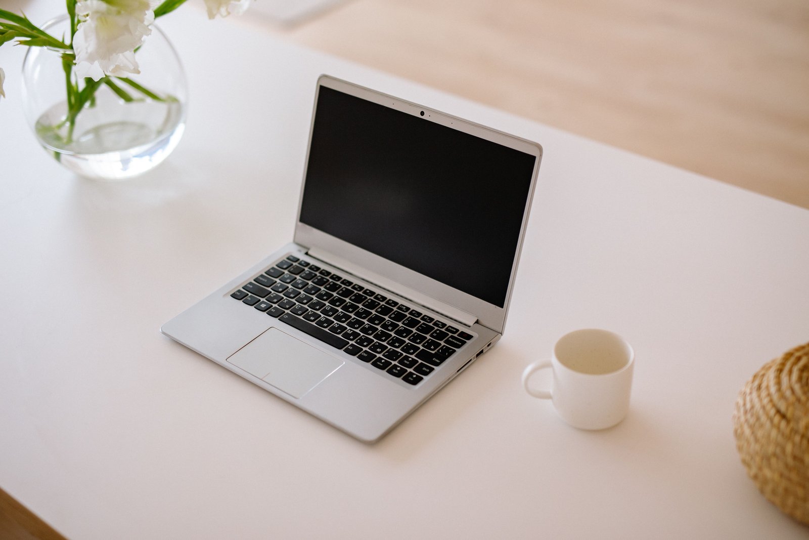 Een opgeruimd bureau bij daglicht met een opengeklapte laptop, een kop koffie en een vaas