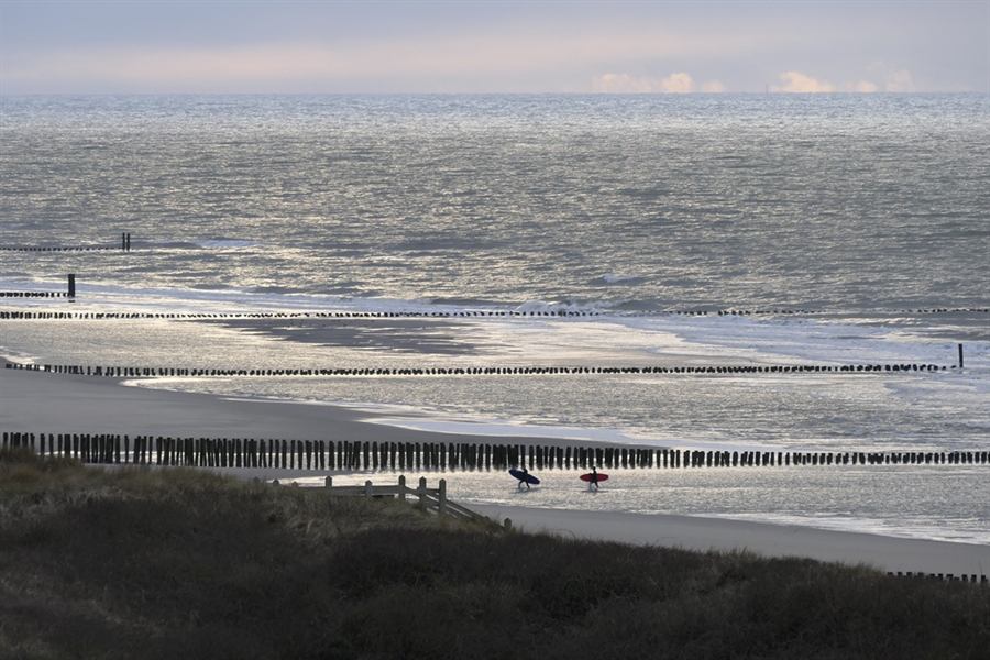 Twee surfers lopen langs de vloedlijn bij Domburg in het tegenlicht