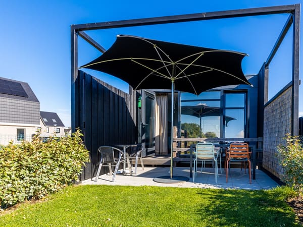 Terras met parasol, tafel en stoelen bij een donker afgewerkt vakantiehuis met tuin