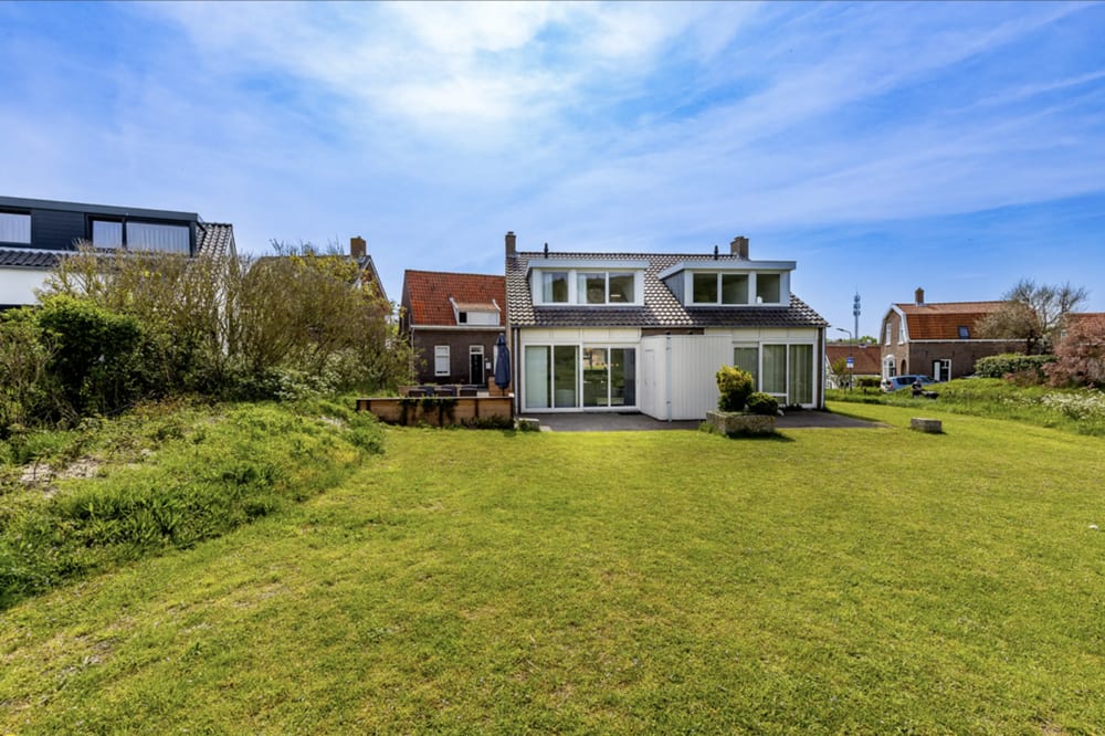 Twee rijen vrijstaande huizen met rode pannendaken achter een grasveld.