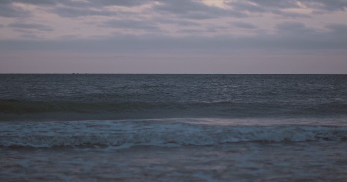 De Noordzee bij schemering, lage golven rollen naar het strand.