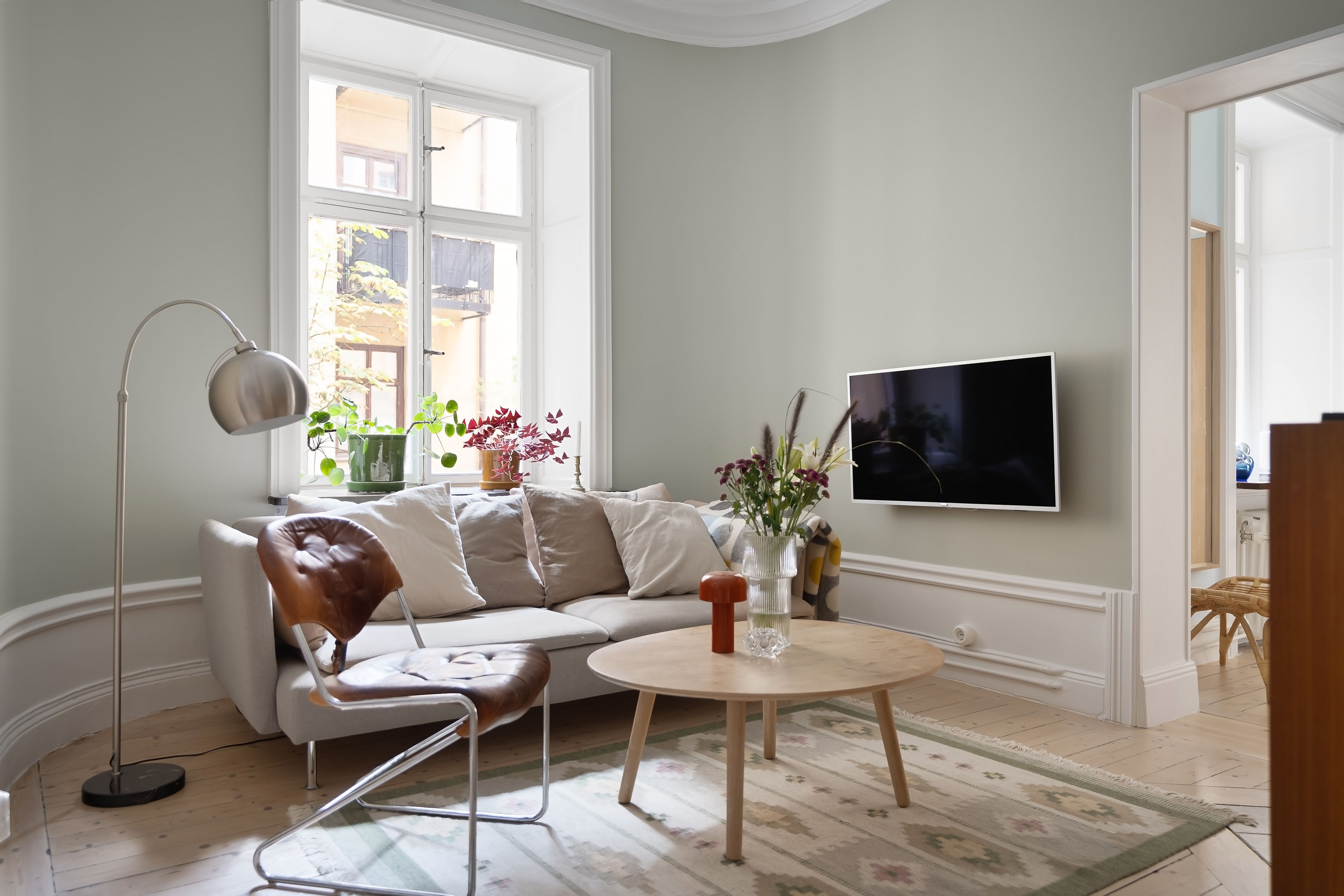 Lichte woonkamer met een linnen bank, houten salontafel en daglicht door een hoog raam.