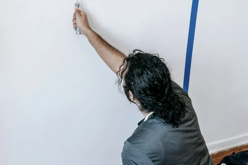 Schilder werkt langs een strak afgeplakte rand met blauwe afplaktape op de muur