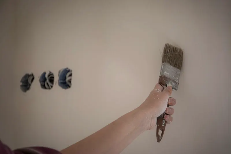 Kwast zet een rand langs stopcontacten op een lichte muur