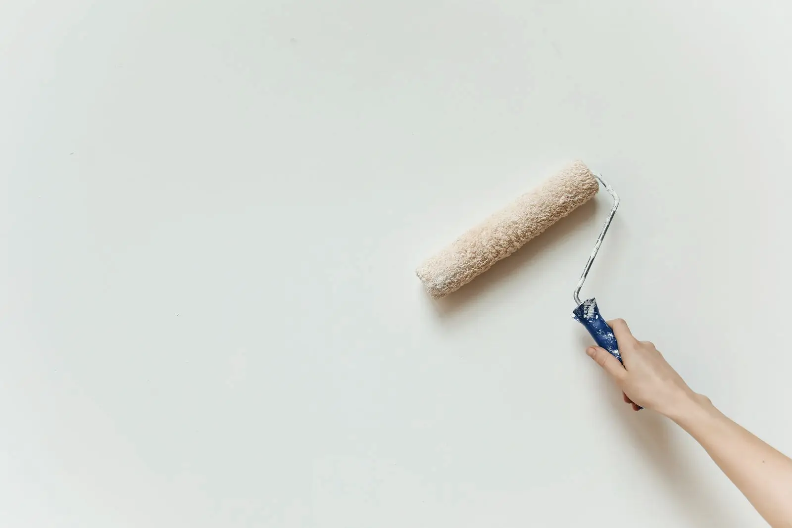 Hand met een verfroller zet een egale laag lichte verf op een gladde wand