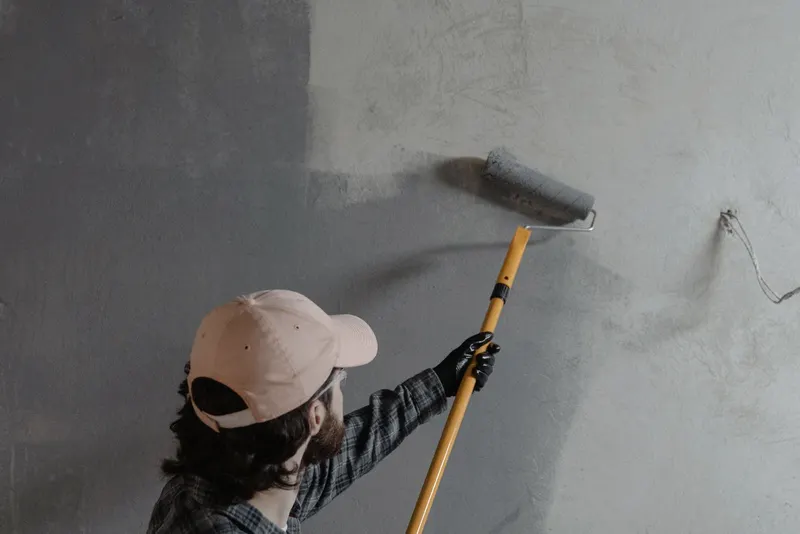 Schilder rolt met een verlengsteel een grote wand in een lege ruimte