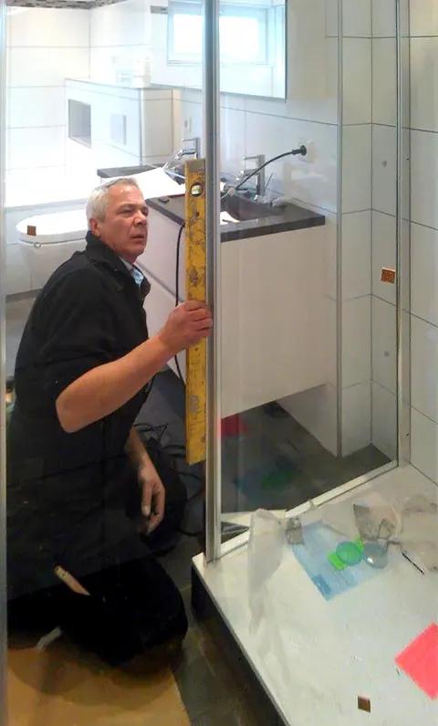 Eric Gobeyn meet met een duimstok in een badkamer met een glazen douchewand