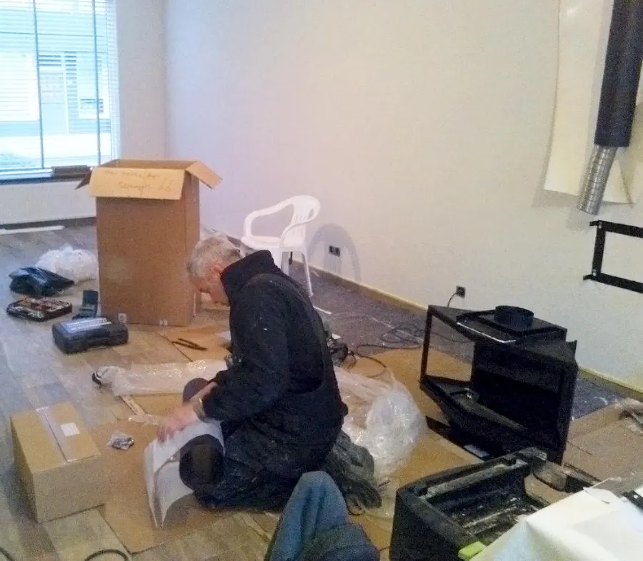Eric Gobeyn werkt geknield aan een vloer tussen gereedschap en verpakt materiaal tijdens een verbouwing