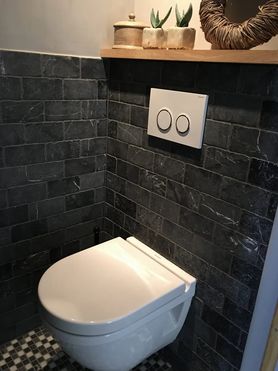 Hetzelfde soort toiletruimte na renovatie, met donkere natuursteenstrips, een hangend closet en een tweeknops bedieningsplaat