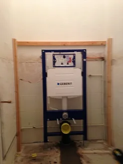 Ingebouwd closetreservoir in een uitgebroken wand, met nieuwe leidingen en een houten omtimmering