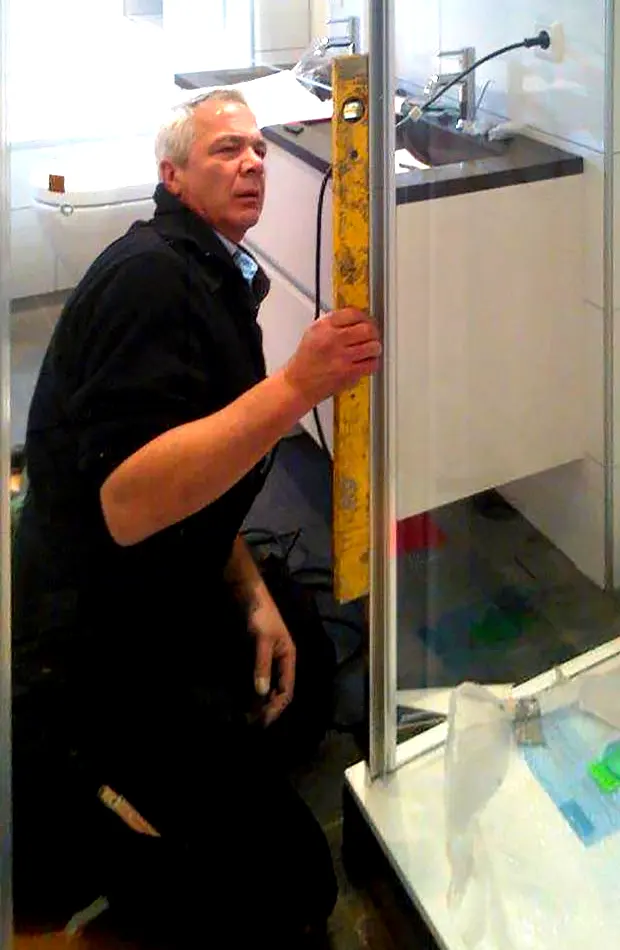 Eric Gobeyn houdt een gele waterpas tegen de stijl van een douchecabine