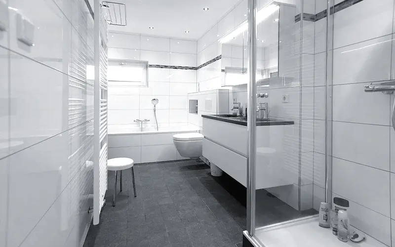 Afgewerkte badkamer met witte wandtegels, ligbad, hangtoilet en een glazen douchecabine