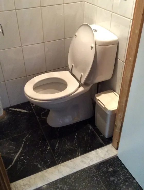 Toilet met beige closet, lichte wandtegels en een donkere marmeren vloer