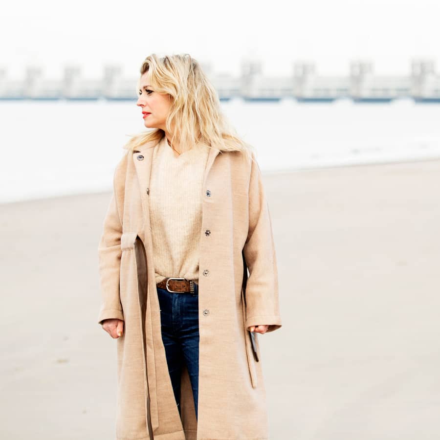Vrouw in een lange jas wandelt langs het water aan de Zeeuwse kust