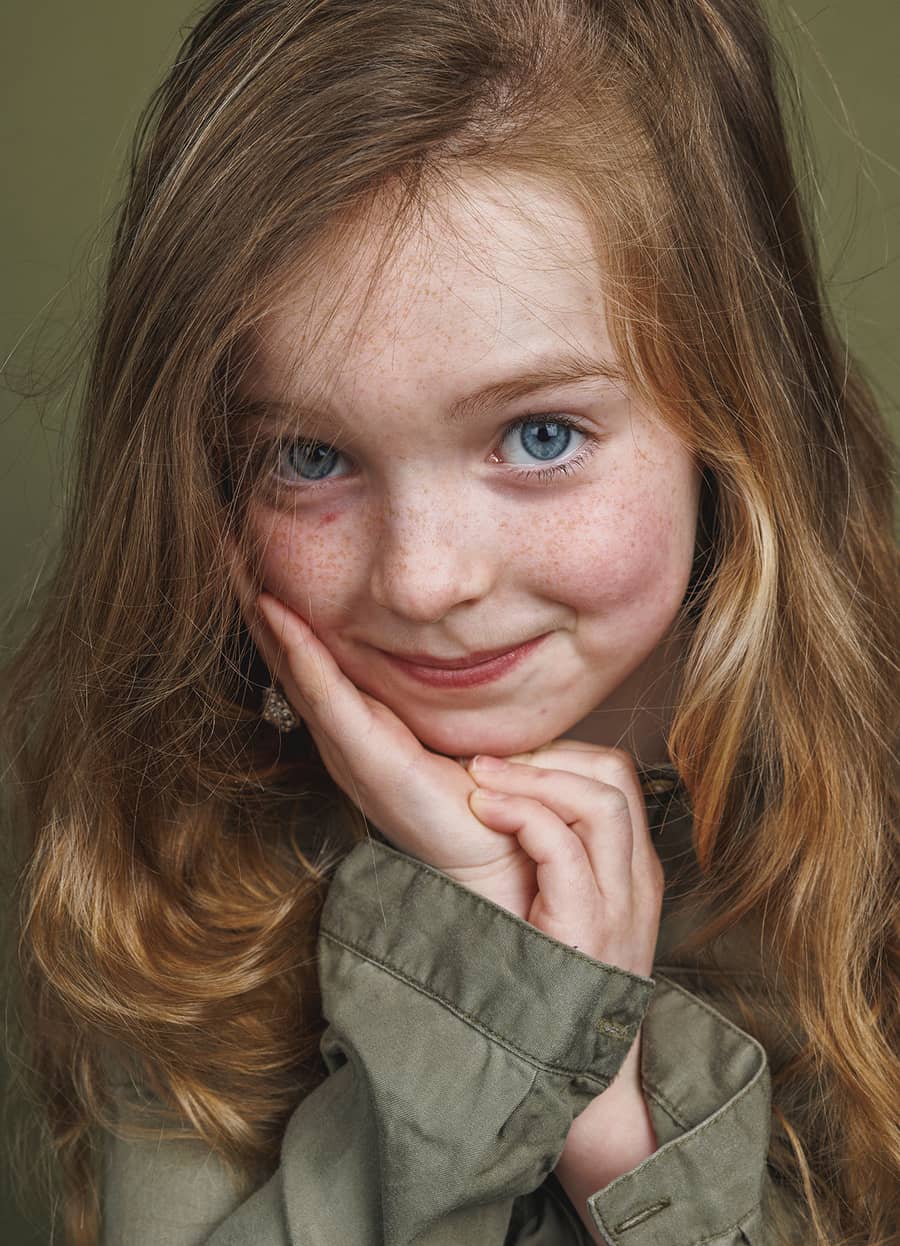 Meisje met haar handen onder haar kin tegen een olijfgroene achtergrond