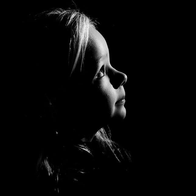 Zijaanzicht van een kind in zwart wit tegen een zwarte achtergrond