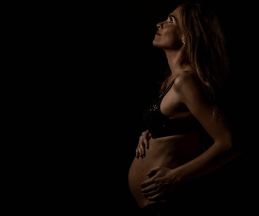 Zwangere vrouw in donker licht tegen een zwarte achtergrond