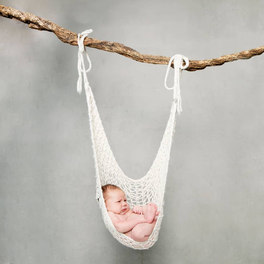 Pasgeboren baby slaapt in een gehaakt hangmatje aan een tak