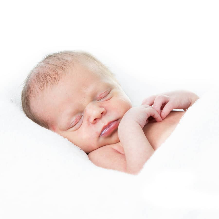 Pasgeboren baby slaapt opgerold op een witte ondergrond
