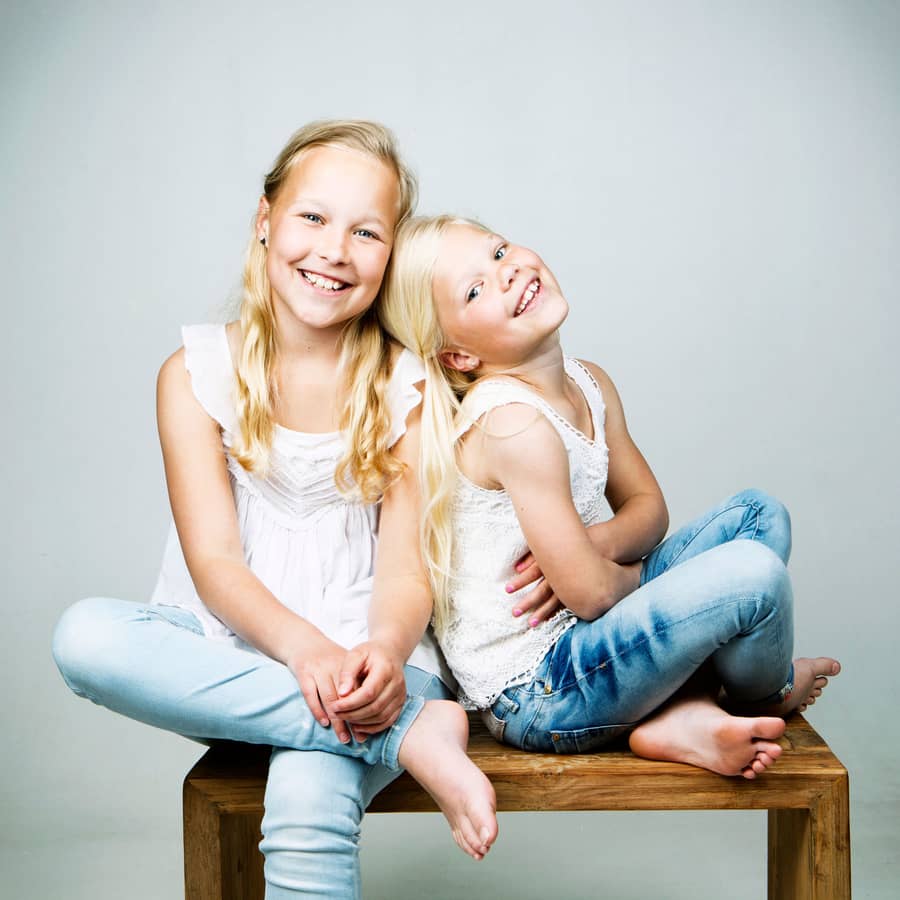 Twee blonde zusjes in witte shirts op een houten bankje