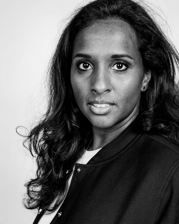 Zwart-witportret van een vrouw met lang donker krullend haar in een donker jack, recht in de lens kijkend.