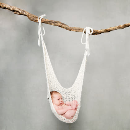 Pasgeboren baby die slaapt in een gehaakte hangmat aan een tak, voor een betonnen wand.