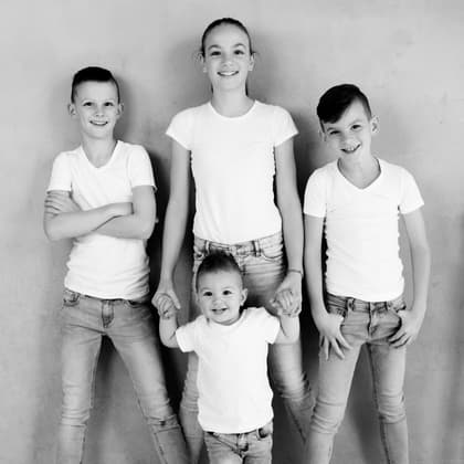 Vier kinderen in witte T-shirts en jeans naast elkaar voor de grijze betonnen wand van de studio.