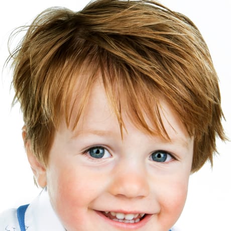 Portret van een jongen met rossig haar in een wit poloshirt, tegen een lichte achtergrond.