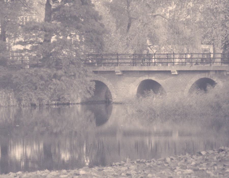 Een gemetselde brug met bogen boven stil water in de herfst