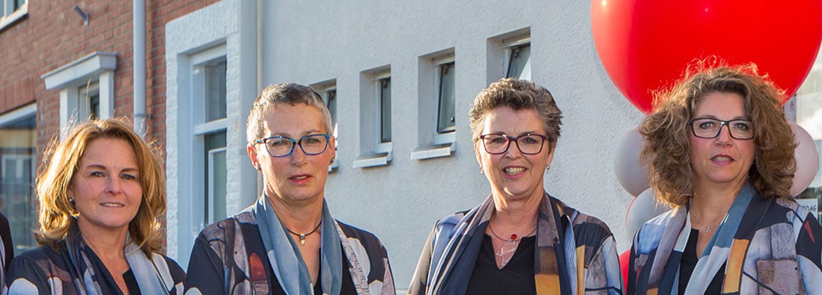Vier vrouwen naast elkaar voor een gevel, met ballonnen