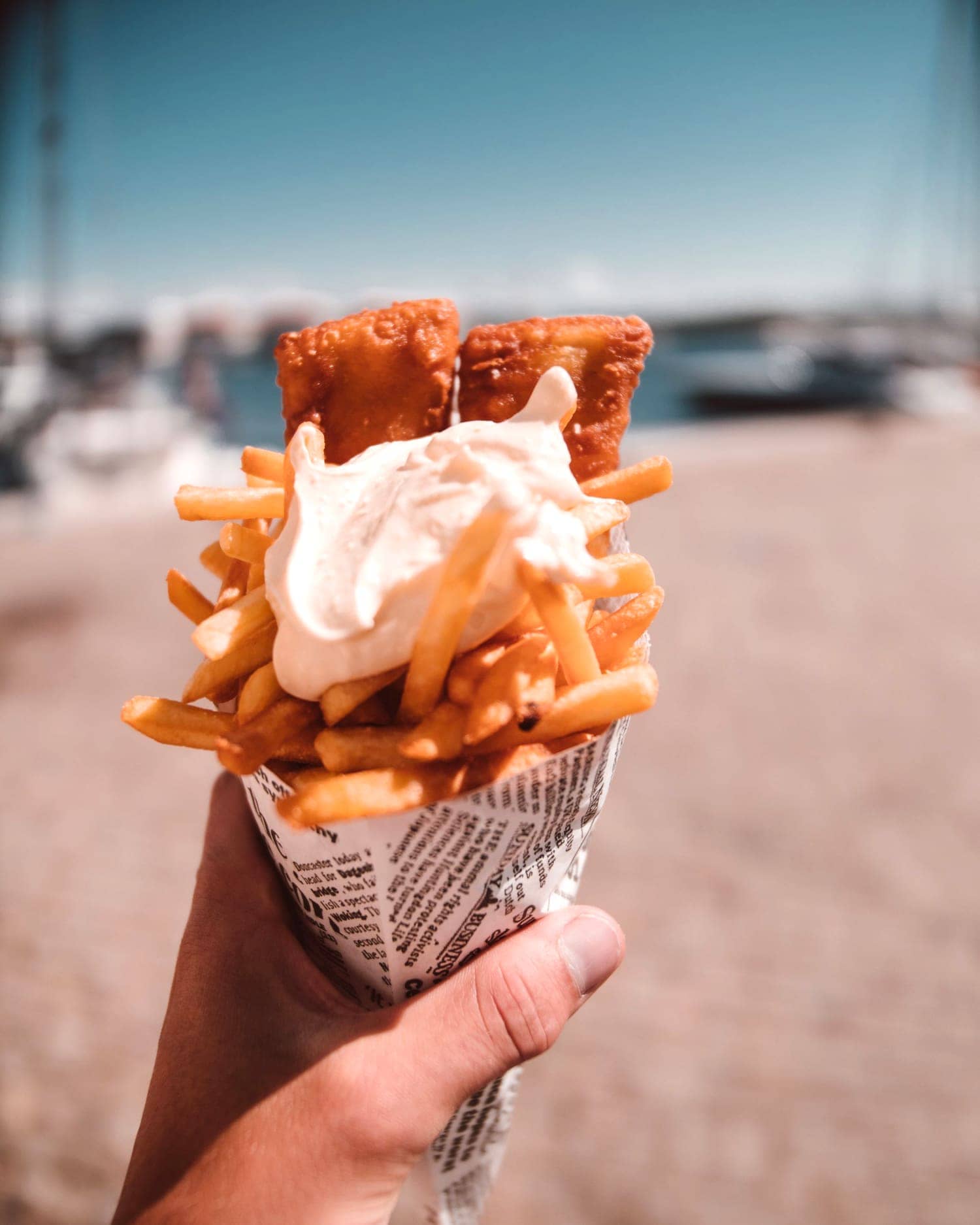 Een puntzak friet met saus, vastgehouden aan zee