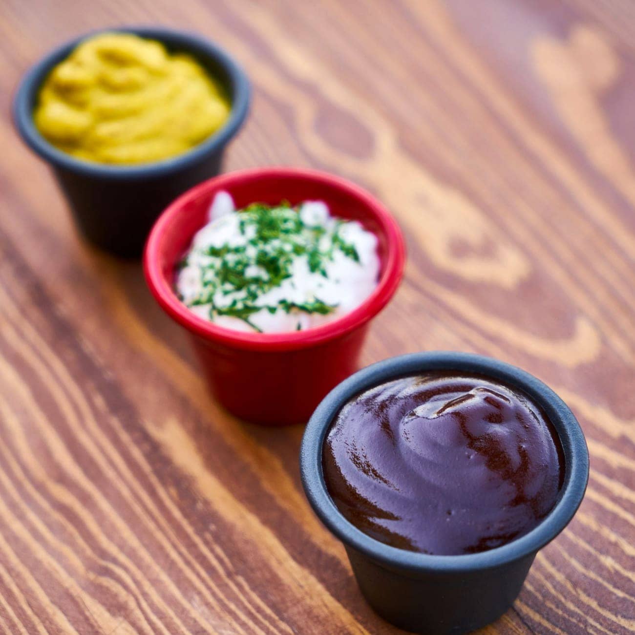 Drie potjes saus in verschillende kleuren op een houten blad