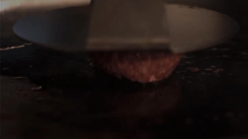 Een burger wordt met een spatel op de hete bakplaat aangedrukt