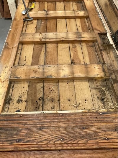Oude houten deur ligt plat in de werkplaats, het hout is verweerd en de verflaag is eraf gehaald.