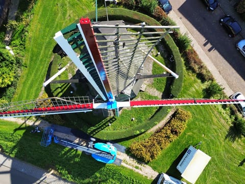 Molen van bovenaf, met pas geschilderde wieken in rood, wit en blauw en een hoogwerker ernaast.