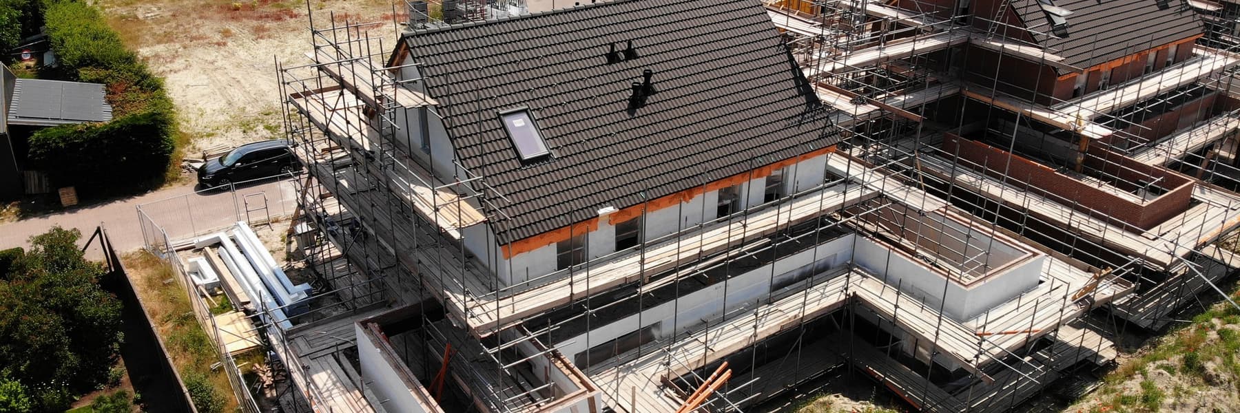Rij woningen in aanbouw van bovenaf gezien, met steigers rondom en een spandoek van Franse langs de weg.