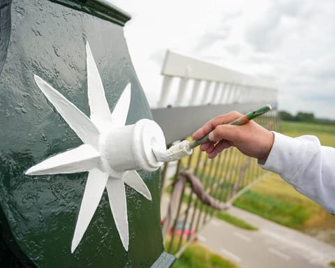Hand met kwast schildert een witte stervormige versiering op de donkergroene romp van een molen.