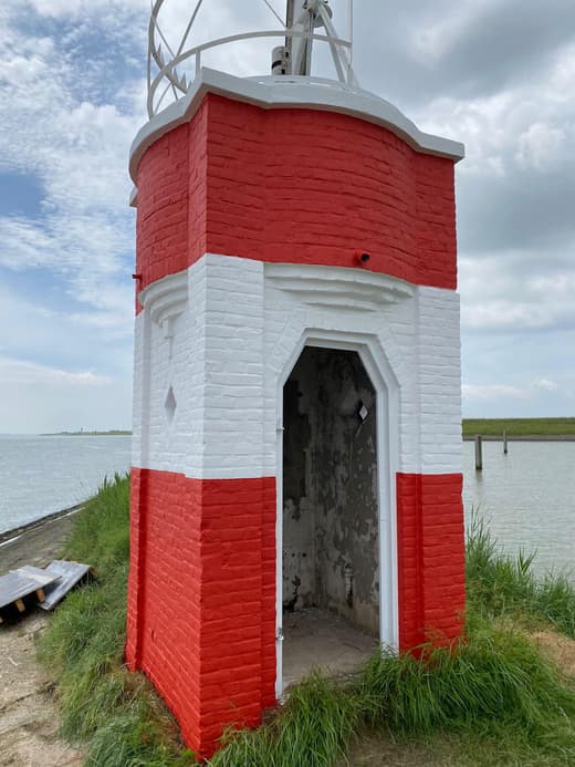 Een klein gemetseld torentje langs het water, rood en wit geschilderd. Door de open deur is de onbehandelde binnenkant te zien.