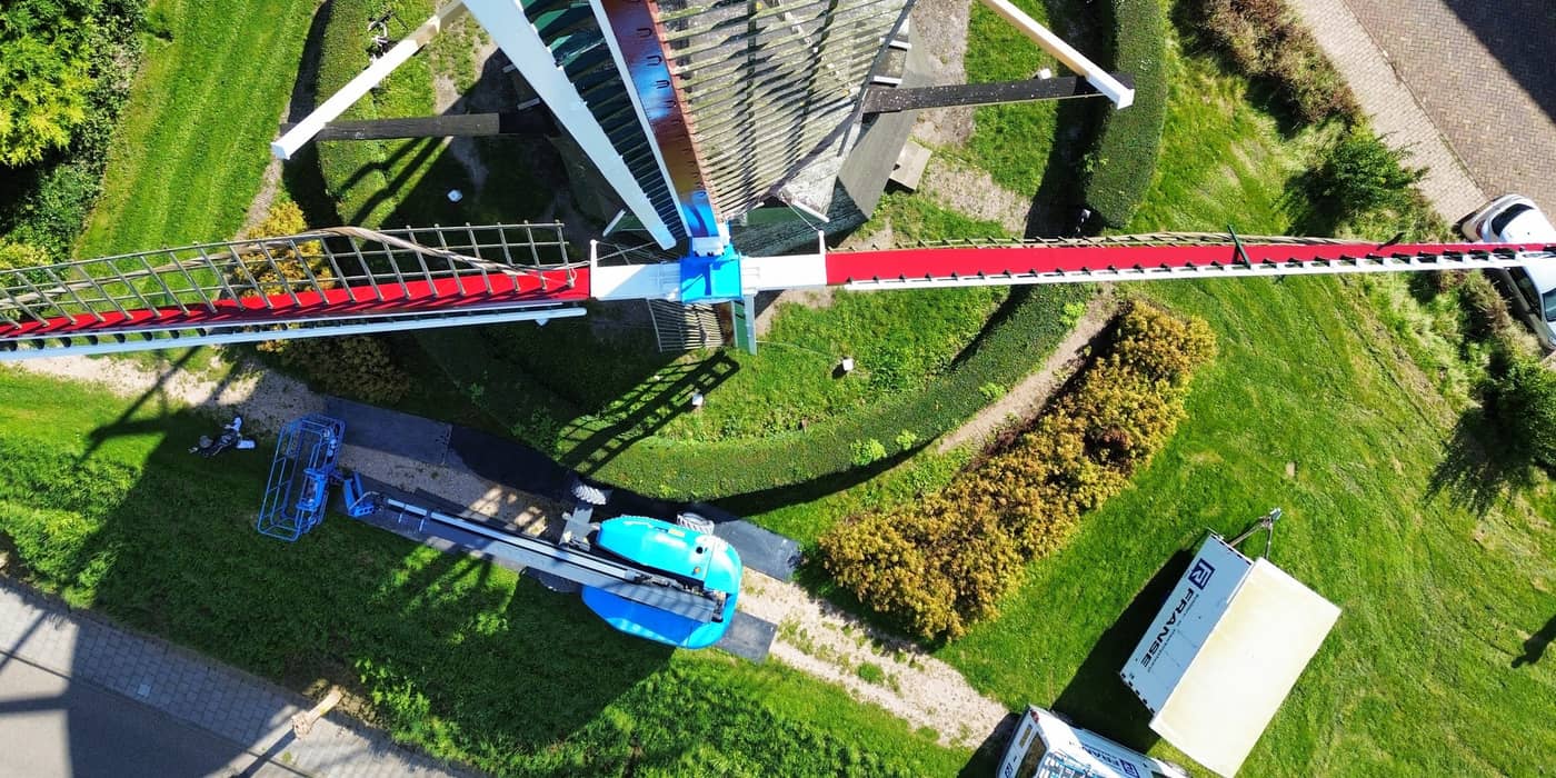 Molenkap met geschilderde roeden, gezien vanuit de lucht. Onder de molen staan een hoogwerker en een bus van Franse.