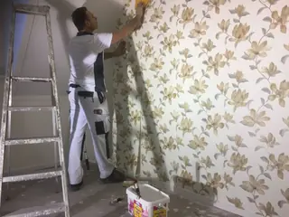 Schilder trekt een baan crème bloembehang recht naast een ladder.