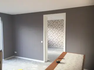Kamer met grijs geschilderde wanden en doorkijk naar een kamer met bloembehang.