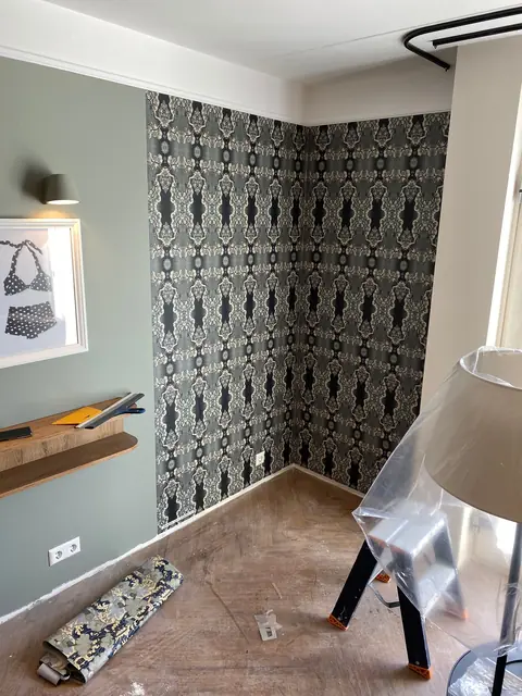 Hoek van een kamer met donker damastbehang naast een zachtgroene wand.